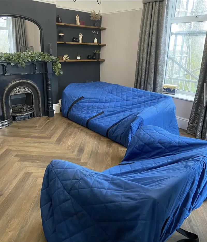 Furniture wrapped in blue quilted covers on a herringbone floor during a Bridge Removals furniture removals job.