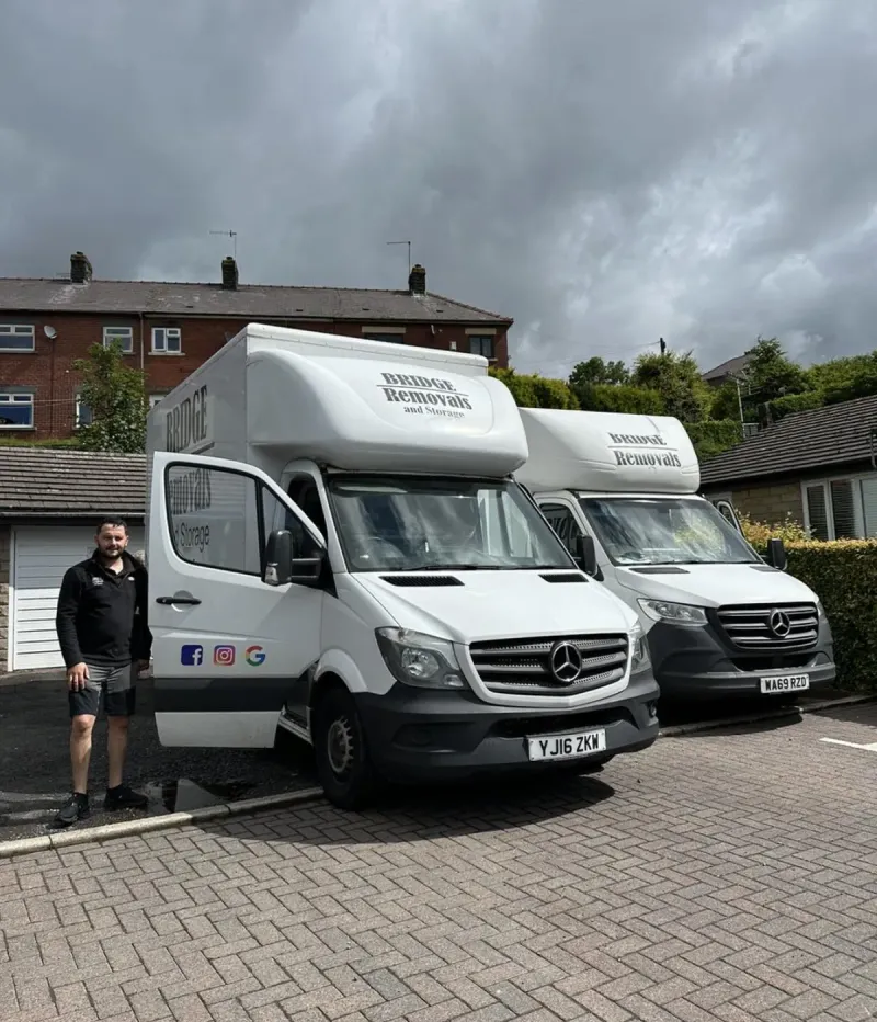 Bridge Removals crew member stands beside two vans under a stormy sky, on a house removals job.