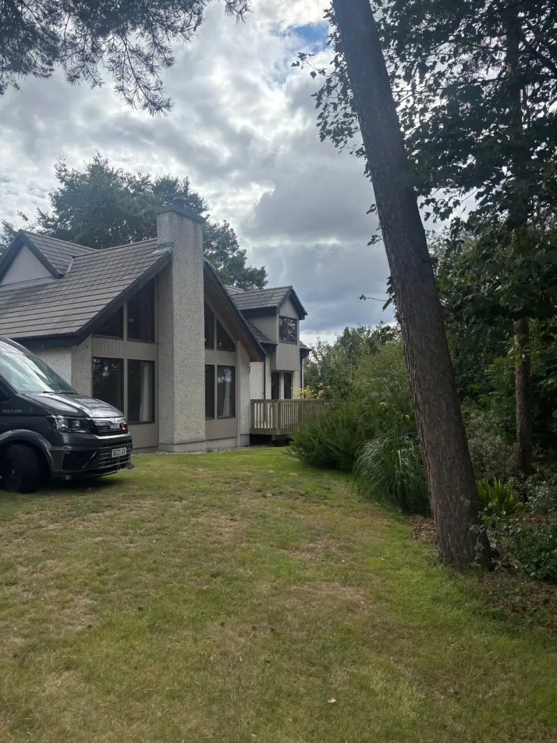 Bridge Removals van parked on the lawn of a chalet-style house among pine trees, midway through a house removals job.