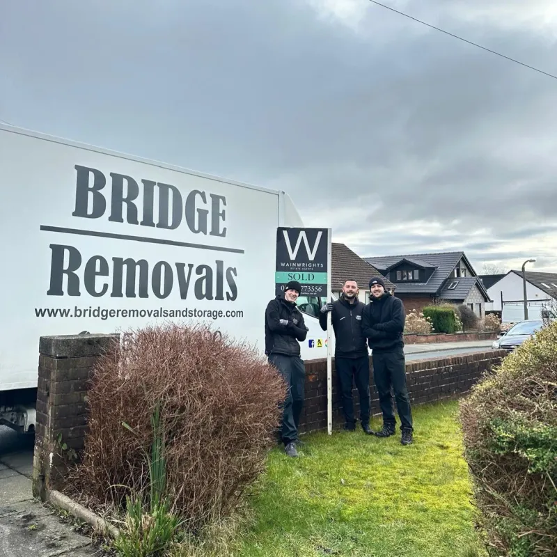 Bridge Removals crew stand beside a Wainwrights SOLD board after finishing a house removals job.
