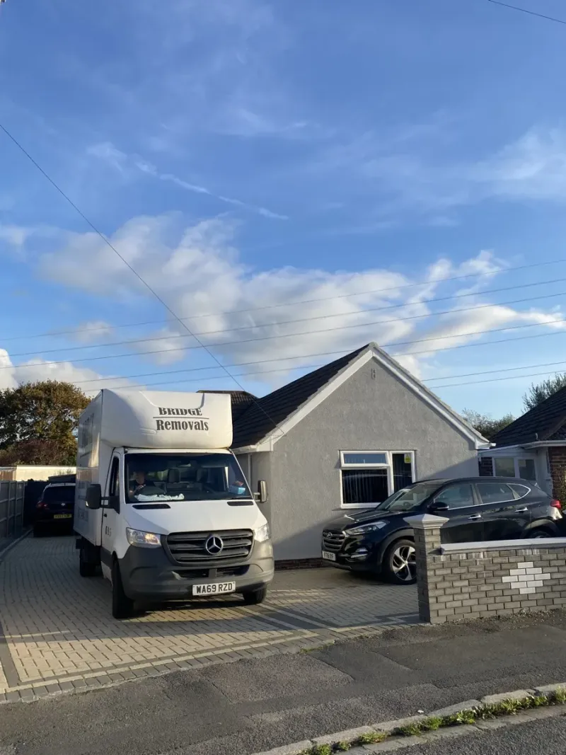 Bridge Removals van outside a grey-rendered bungalow next to a black SUV, on a house removals job.