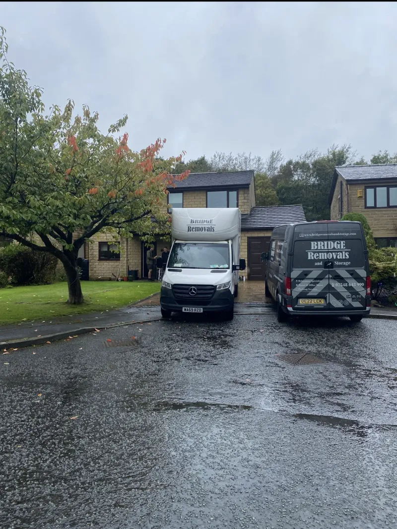 Two Bridge Removals vans outside a stone house on a wet autumn house removals job.