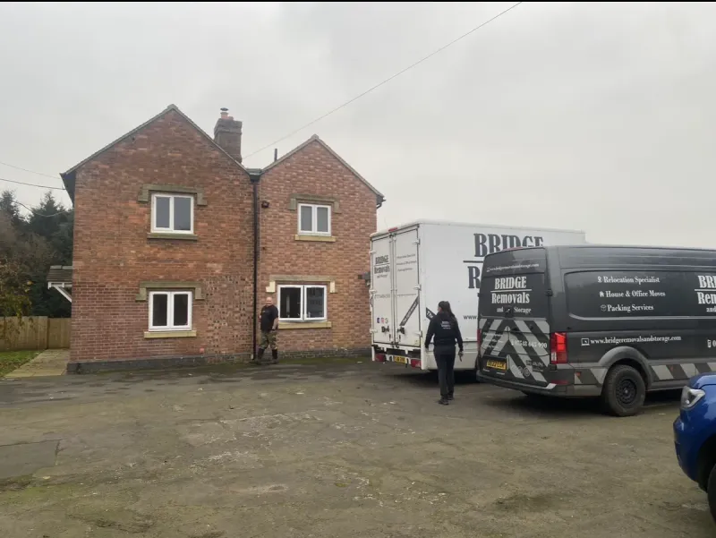 Bridge Removals van on a house move at a red brick farmhouse, crew members crossing the yard