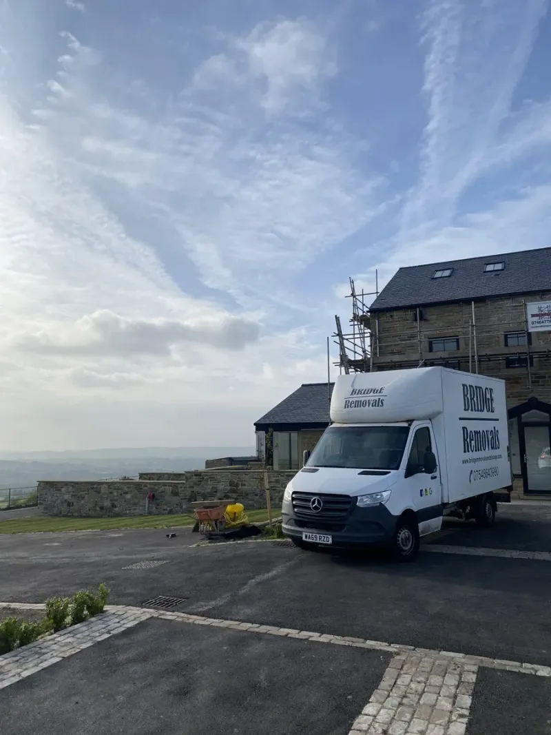 Bridge Removals van at a hilltop stone house with scaffolding in Accrington, valley view behind, on a house removals job.