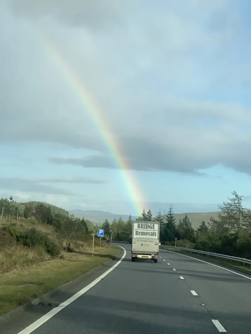 Bridge Removals lorry driving a rural moorland road under a vivid rainbow, en route on a house removals job.