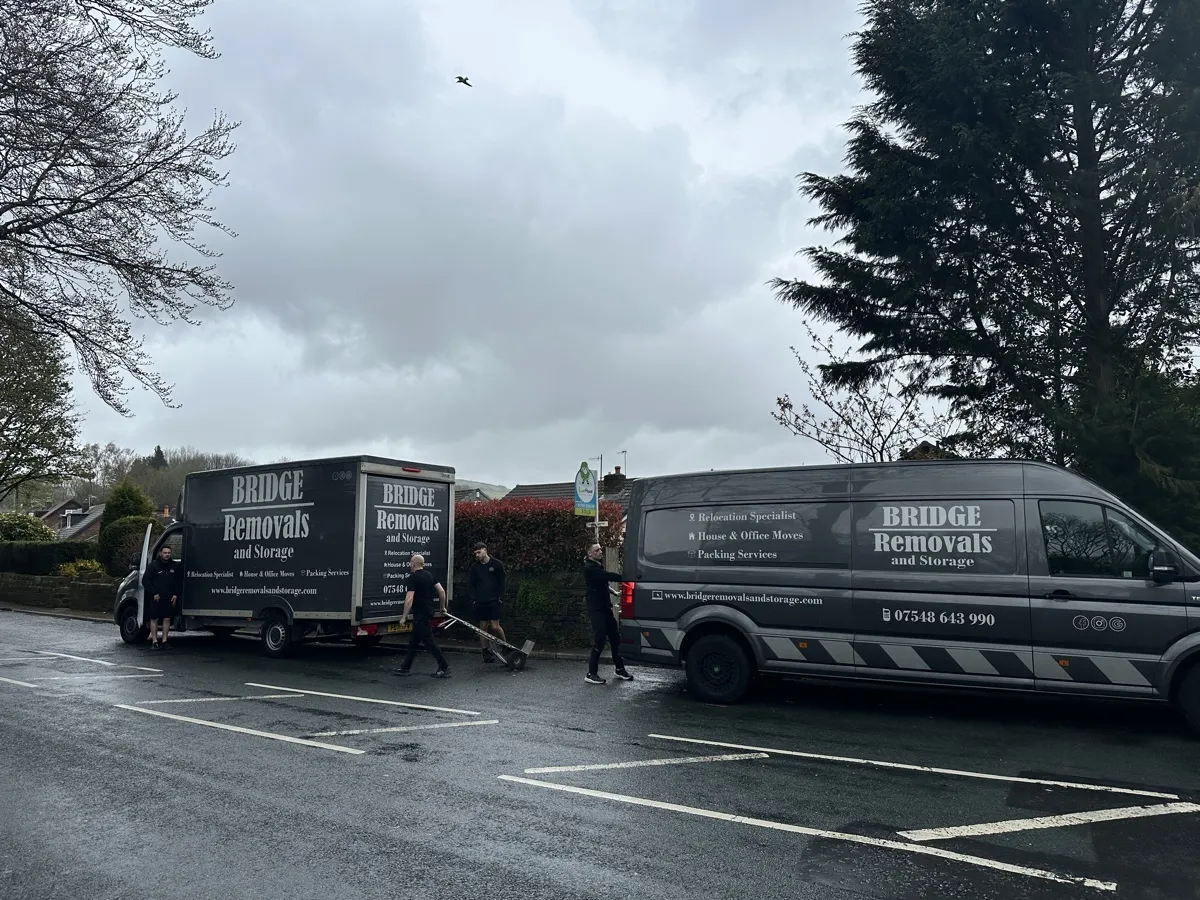 House Removals on a Wet Road Bridge Removals crew move items between two vans on a wet tree-lined road, out on a house removals job.