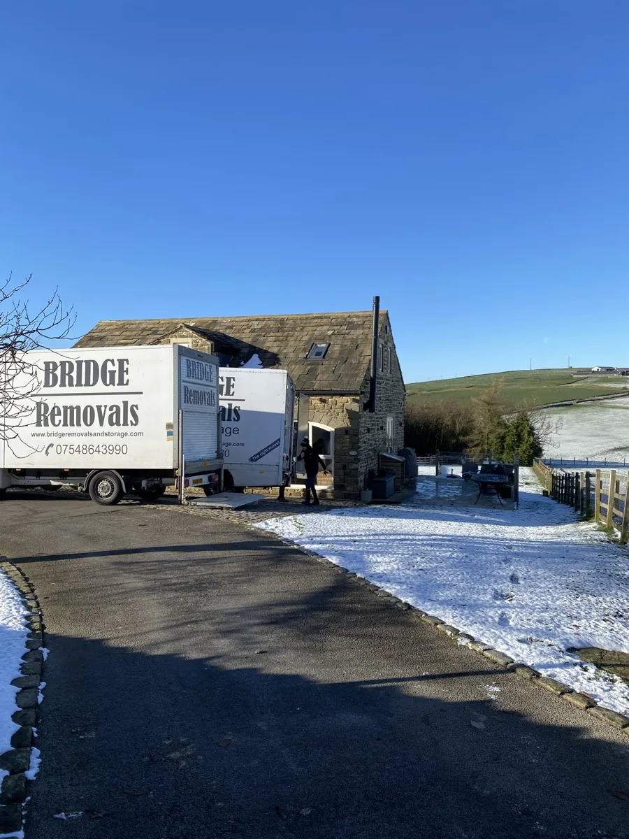 House Removals in the Snow Two Bridge Removals vans parked outside a snow-covered stone house, on a house removals job.