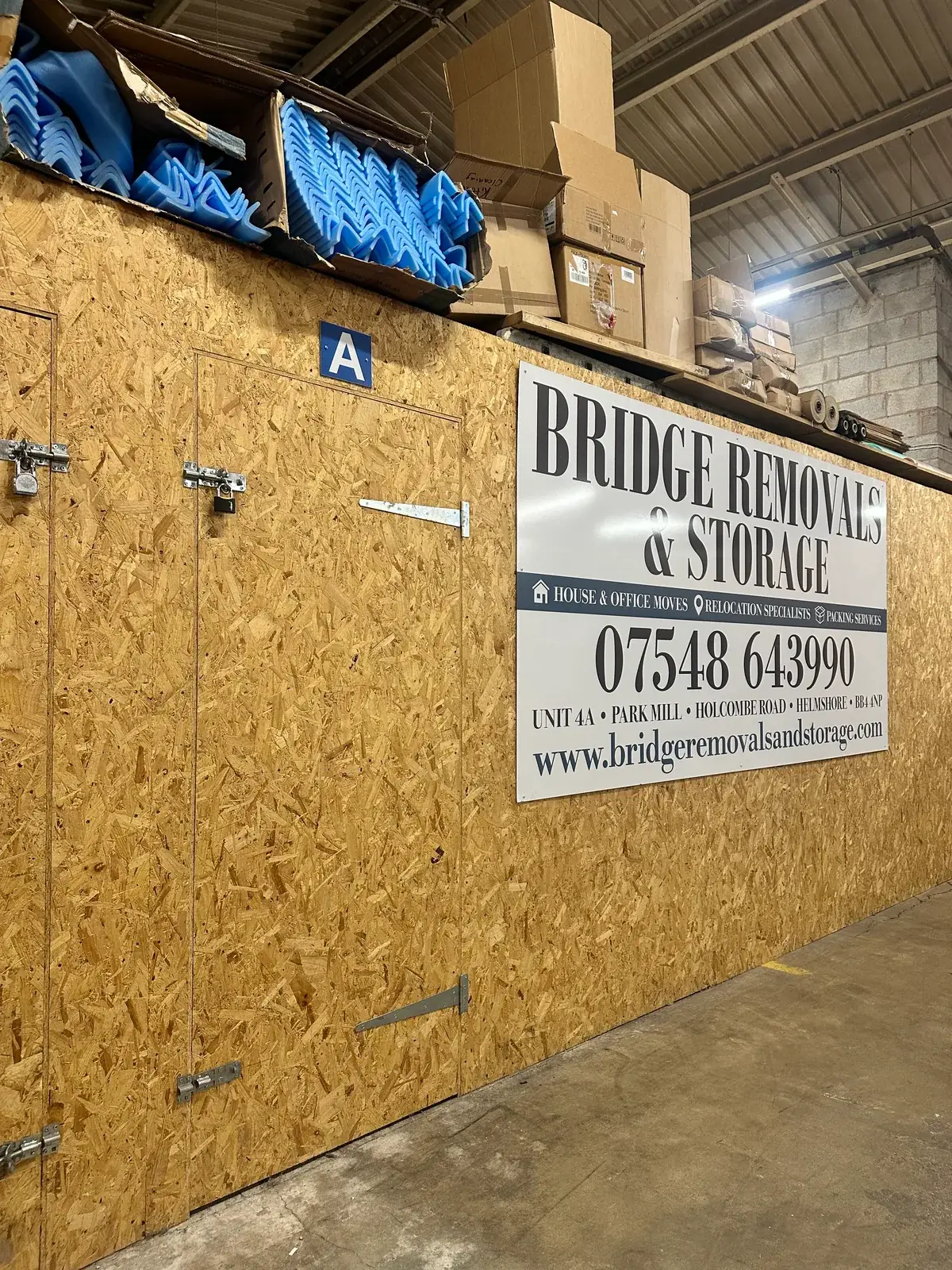 Bridge Removals & Storage signage above the units in Helmshore, packing boxes stacked nearby