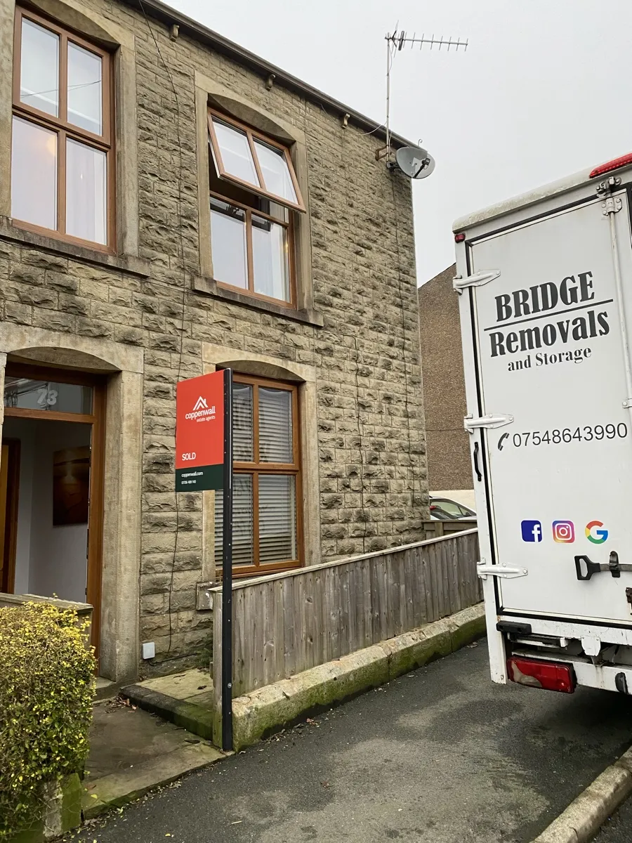 Haslingden Terrace House Sold And Moved Bridge Removals van pulled up tight to a stone terrace in Haslingden, a SOLD board out front, on a house removals job.