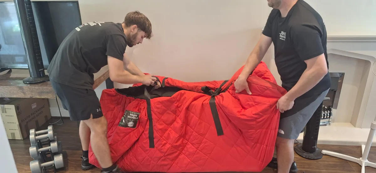 Customer-submitted photo showing Bridge Removals crew wrapping furniture in a red padded cover