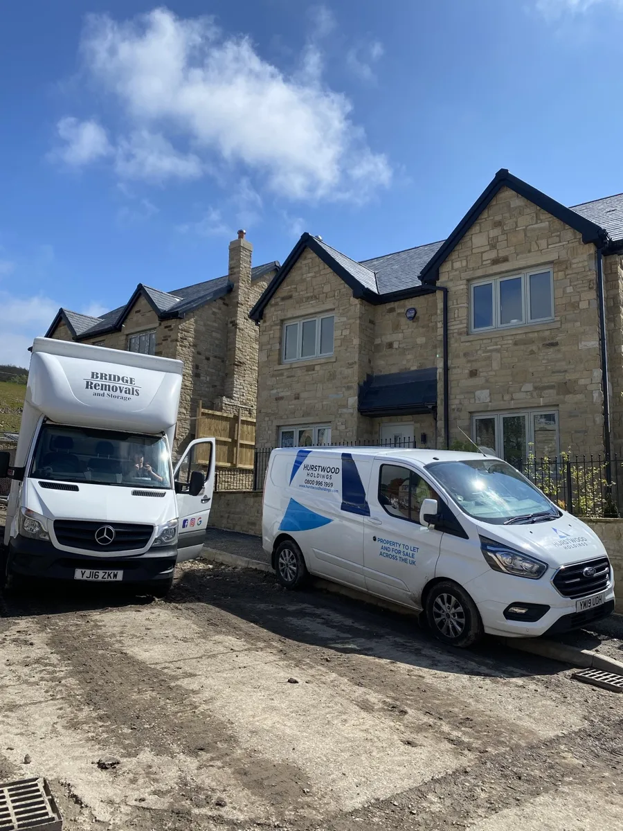 Cloughfold New Build House Move Bridge Removals van beside a Hurstwood Holdings van outside a new-build stone house in Cloughfold on a house removals job.