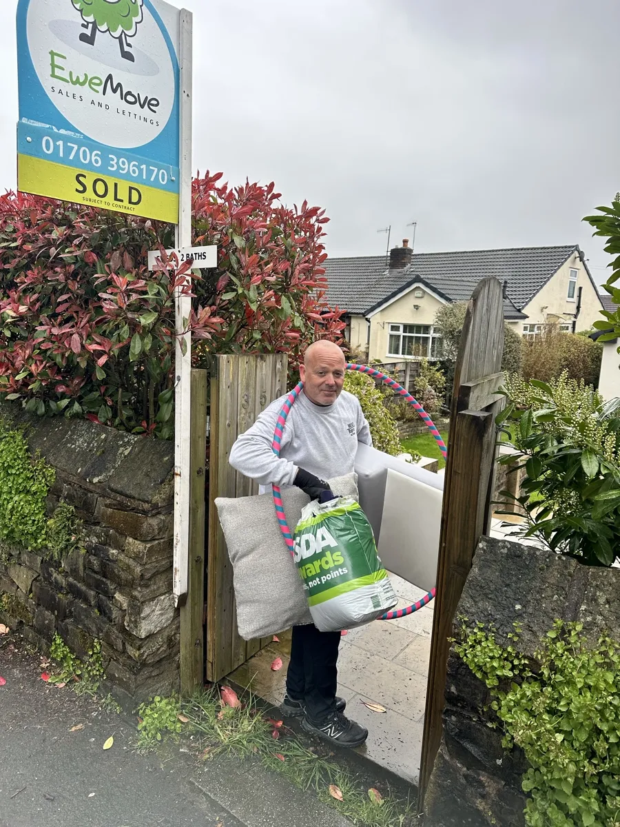 House Removals Under an EweMove Sold Sign Bridge Removals crew member carries a hula hoop and cushion past an EweMove SOLD sign, on a house removals job.