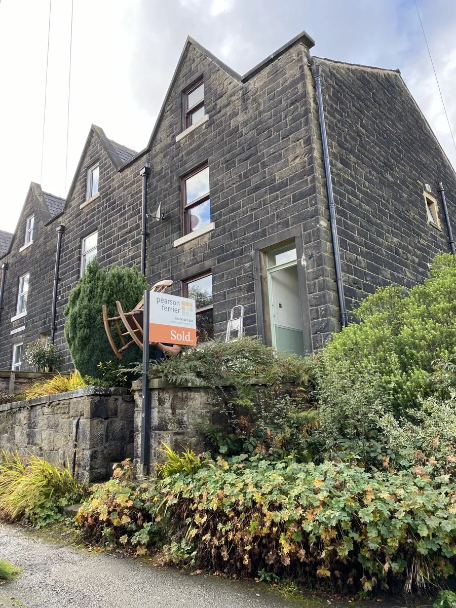Bridge Removals moves a chair past a Stubbins terrace, Pearson Ferrier's sold board nearby, on a house removals job.