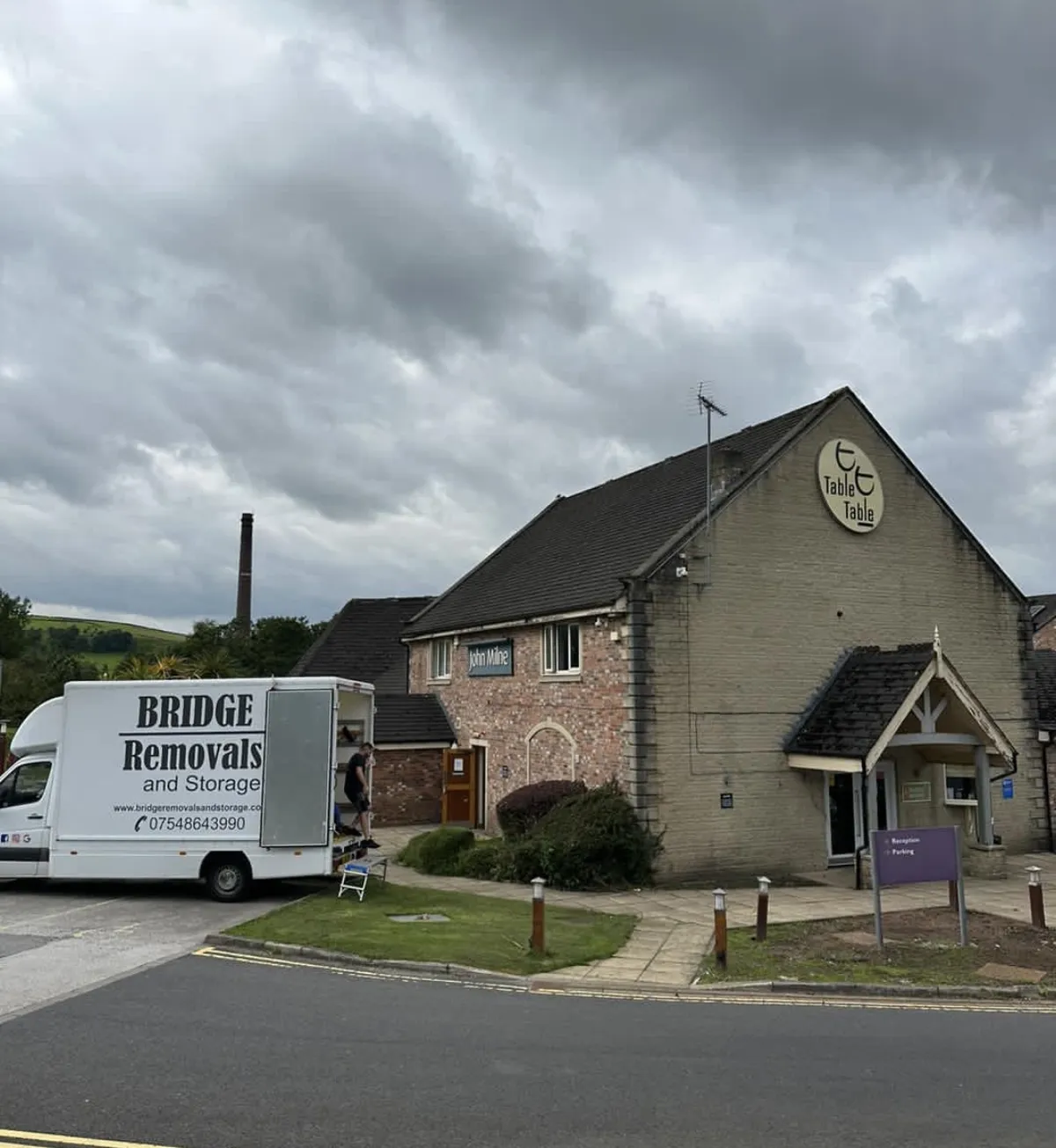 Bridge Removals van parked outside a pub and restaurant during a furniture removals job, storm clouds overhead.