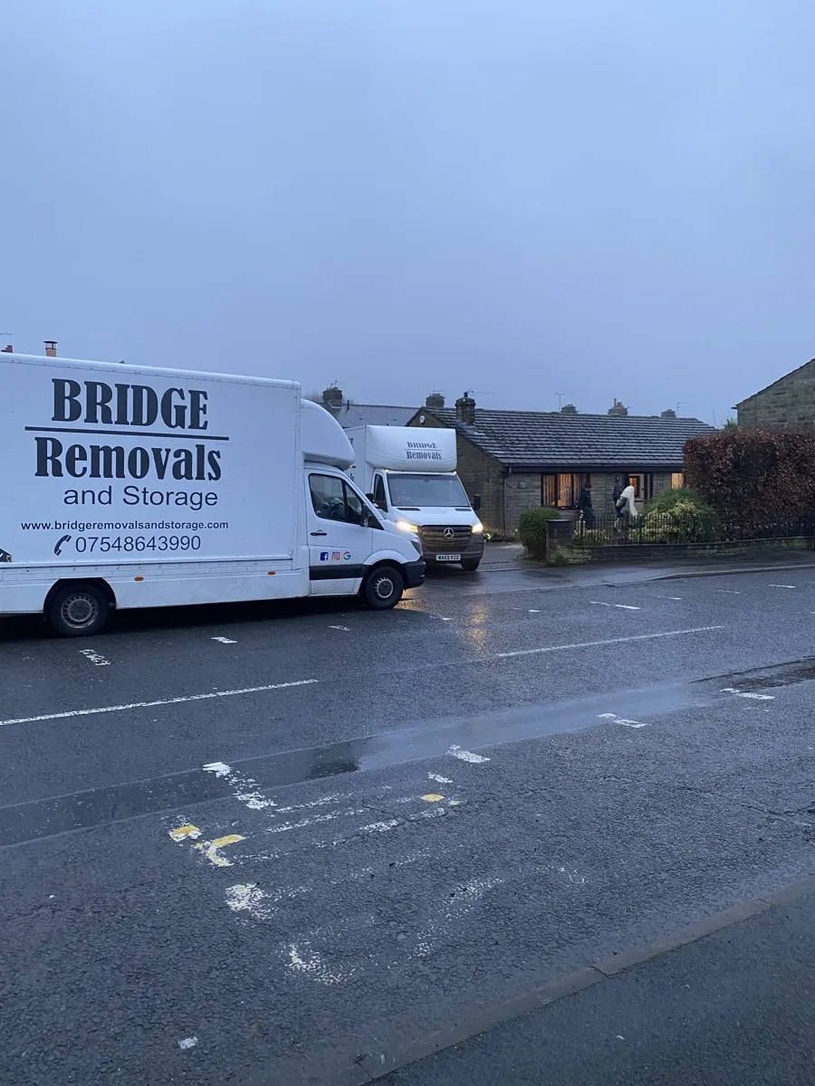 Loveclough Bungalow Move At Dusk Bridge Removals vans with headlights on outside a stone bungalow in Loveclough on a wet evening house removals job.